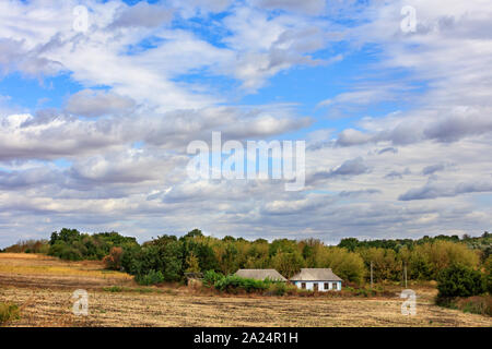 Ein verlassenes Landhaus steht auf der Seite einer ländlichen Straße am Rande eines Feldes unter einem bewölkten Himmel. Stockfoto