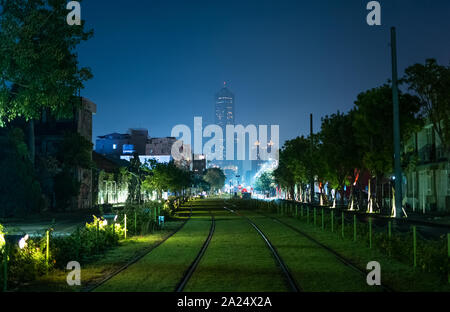 Kaohsiung, Taiwan: Blick auf die grünen Gras bedeckt Kaohsiung Light Rail Zug in Richtung Tuntex Sky Tower 85 im Stadtzentrum in der Nacht führt. Stockfoto