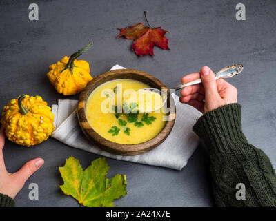 Frauen Hände, die heiße Sahne hausgemachtem Kartoffel- und Kürbissuppe auf dem grauen Tabelle, Ansicht von oben. Stockfoto