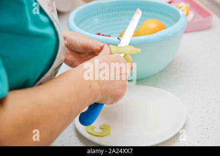 Direkt oberhalb der Schoß der Frau Peeling ein Apple. Die Frau klopft oben auf dem Apple. Weibliche Hände Peeling Haut aus der Green Apple mit einem Schälbohrer Stockfoto