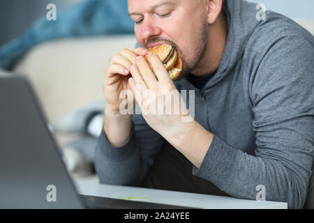 Mann sitzen auf dem Sofa und Burger essen gegen flach Stockfoto