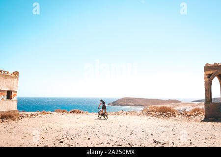 Person auf dem Mountainbike Fahrrad in der Landschaft der Wüste in der Nähe der Küste mit Blick auf das Meer im Hintergrund Stockfoto