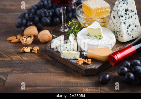 Käseplatte mit Trauben, Honig, Nüsse und Rotwein auf einem Holztisch. Stockfoto