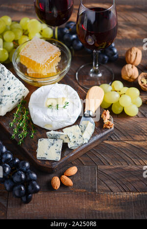 Käseplatte mit Trauben, Honig, Nüsse und Rotwein auf einem Holztisch. Stockfoto