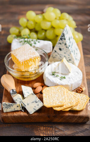 Käseplatte mit Trauben, Cracker, Honig und Nüssen auf einem Holztisch. Stockfoto