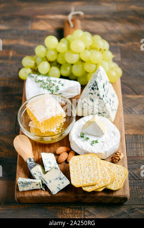 Käseplatte mit Trauben, Cracker, Honig und Nüssen auf einem Holztisch. Stockfoto