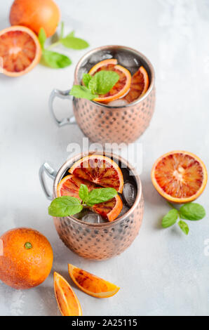 Blutorange Moscow Mule Alkohol Cocktail mit frischen Minzeblättchen und Eis in Kupfer Tassen auf grauem Beton Hintergrund. Stockfoto