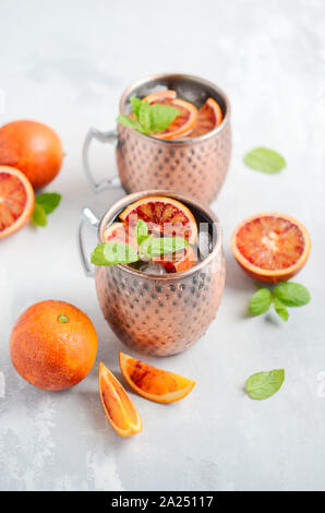 Blutorange Moscow Mule Alkohol Cocktail mit frischen Minzeblättchen und Eis in Kupfer Tassen auf grauem Beton Hintergrund. Stockfoto