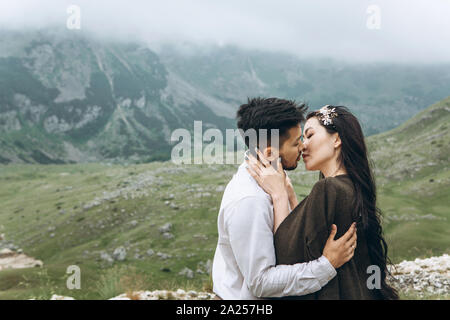 Ein Mann und eine Frau sanft umarmt sie küssen Auf die Natur vor dem Hintergrund einer Berglandschaft. Stockfoto