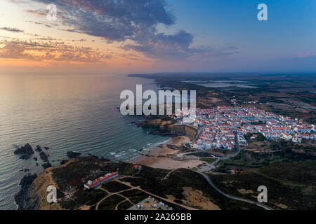 Luftaufnahme der Zambujeira do Mar Dorf und Strand bei Sonnenuntergang, im Alentejo, Portugal; Stockfoto