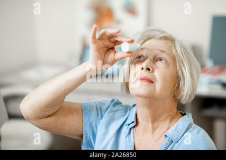 Ältere Frau tropft etwas Medizin mit Tropfenzähler auf ihre Augen an der ophthalmologischen Büro. Konzept der Behandlung mit Augentropfen Stockfoto