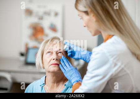Ärztin tropfen Augentropfen auf die Augen eines älteren Patienten während einer Behandlung in der ophthalmologischen Büro Stockfoto