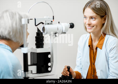 Fröhliche Augenarzt die Augen eines älteren Patienten mit Mikroskop während einer medizinischen Untersuchung in der ophthalmologischen Büro Stockfoto
