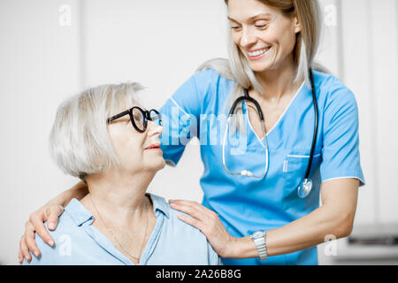 Krankenschwester kümmert sich um ältere Frau, ihre Schultern in der Klinik oder zu Hause umarmen für Ältere Stockfoto