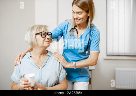 Krankenschwester kümmert sich um ältere Frau, ihre Schultern in der Klinik oder zu Hause umarmen für Ältere Stockfoto