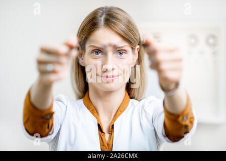 Augenarzt bietet Ihnen Brillen, die auf die Kamera, vor Auge Diagramm ansehen in der Arztpraxis Stockfoto