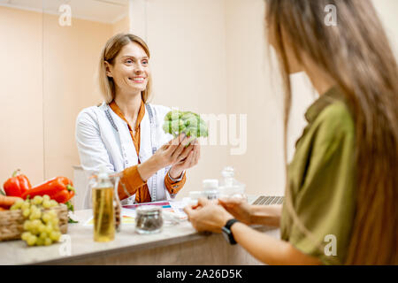 Ernährungssachversta5ndiger mit junge Frau client sprechen über Speisen und gesunde Produkte während einer medizinischen Beratung im Büro Stockfoto