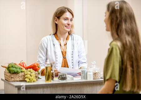 Ernährungssachversta5ndiger mit junge Frau client sprechen über Speisen und gesunde Produkte während einer medizinischen Beratung im Büro Stockfoto