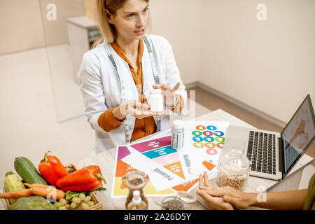 Ernährungssachversta5ndiger mit junge Frau client sprechen über Speisen und gesunde Produkte während einer medizinischen Beratung im Büro Stockfoto