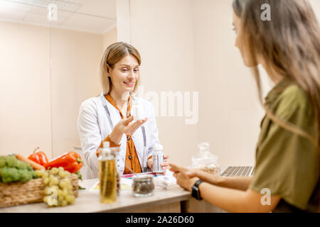 Ernährungssachversta5ndiger mit junge Frau client sprechen über Speisen und gesunde Produkte während einer medizinischen Beratung im Büro Stockfoto