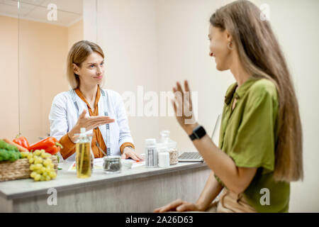 Ernährungssachversta5ndiger mit junge Frau client sprechen über Speisen und gesunde Produkte während einer medizinischen Beratung im Büro Stockfoto