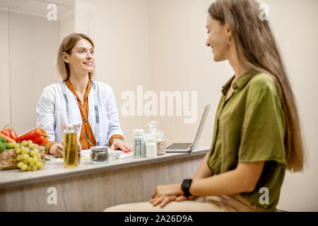 Ernährungssachversta5ndiger mit junge Frau client sprechen über Speisen und gesunde Produkte während einer medizinischen Beratung im Büro Stockfoto