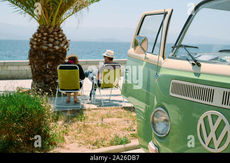 Ein Paar genießt die Aussicht aus Ihrem Retro Vintage classic VW T2 Wohnmobil an der Riviera Küste neben einer Palme im Sommer Stockfoto