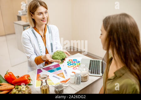 Ernährungssachversta5ndiger mit junge Frau client sprechen über Speisen und gesunde Produkte während einer medizinischen Beratung im Büro Stockfoto