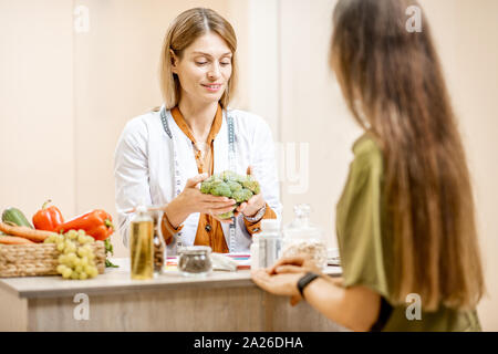 Ernährungssachversta5ndiger mit junge Frau client sprechen über Speisen und gesunde Produkte während einer medizinischen Beratung im Büro Stockfoto