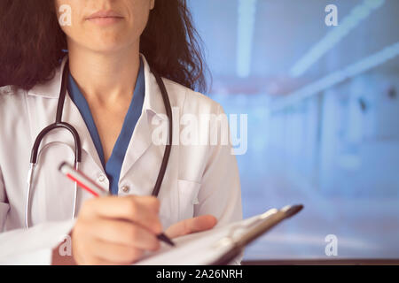 Frau Doktor schreibt Notizen in der Zwischenablage in der Klinik Stockfoto