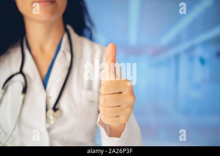 Jungen gutaussehenden Arzt Frau mit Stethoskop über Krankenhaus Hintergrund zur Genehmigung tun positive Geste mit der Hand, Daumen hoch lächelnd und glücklich für s Stockfoto