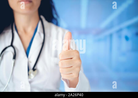 Jungen gutaussehenden Arzt Frau mit Stethoskop über Krankenhaus Hintergrund zur Genehmigung tun positive Geste mit der Hand, Daumen hoch lächelnd und glücklich für s Stockfoto