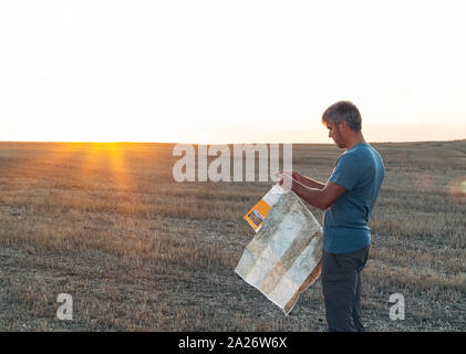 Ein verlorener Mann in der Mitte des Feldes konsultiert eine Karte bei Sonnenuntergang. Lifestyle Konzept Stockfoto