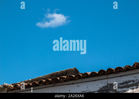 Dach von einem kleinen Haus, mit alten aus weißen Fassade geschält. Strahlend blauen Himmel mit weißen Wolken. Ribeira Grande, Sao Miguel, Azoren, Portugal. Stockfoto