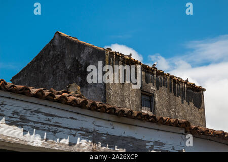 Dach von einem kleinen Haus, mit alten aus weißen Fassade geschält. Strahlend blauen Himmel mit weißen Wolken. Ribeira Grande, Sao Miguel, Azoren, Portugal. Stockfoto