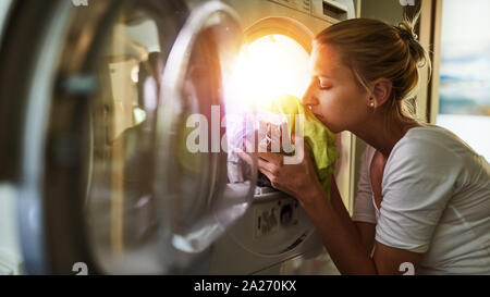 Frau an Hausarbeit riecht an frische Kleider aus dem Wäschetrockner Stockfoto