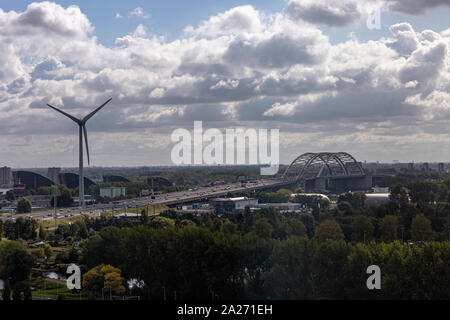 Bewölkten Tag mit blauem Himmel und Wolken über eine städtische Landschaft mit einem Windenergie Windmühle und Verkehr über ein Bügeleisen Bau Brücke Stockfoto