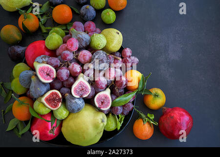 Luftaufnahme frisches Obst auf einem dunklen Hintergrund. Violetten und grünen Feigen, Granatäpfel, Trauben, Birnen und Orangen. Stockfoto