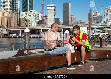 07.05.2018, Sydney, New South Wales, Australien - zwei Arbeiter nehmen eine Mittagspause in Darling Harbour, während die Skyline des Geschäftsviertels werden kann Stockfoto