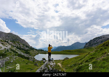 Weibliche Bergsteiger steht auf einem Boulder und fotografiert die Landschaft in den Dolomiten in Italien mit Ihrem Mobiltelefon Stockfoto