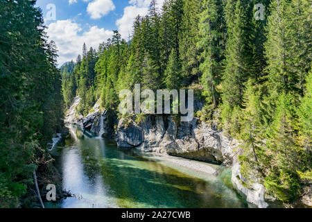 Horizontale Sicht auf eine idyllische Landschaft mit einem Bergsee und kleinen Wasserfall von grünen Pinienwald umgeben Stockfoto