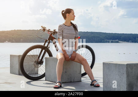 Fitness Mädchen in kurzen weißen Shorts in der Nähe von See mit Fahrrad im City Park. Gesundheit, Sport, Reisen Stockfoto