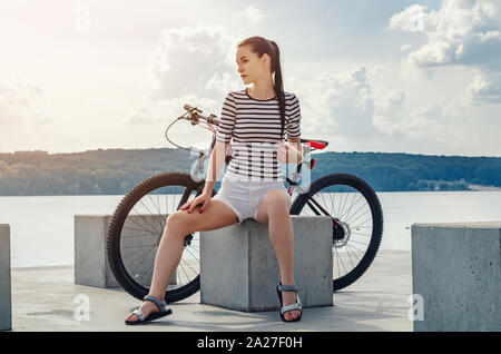 Fitness Mädchen in kurzen weißen Shorts in der Nähe von See mit Fahrrad im City Park. Gesundheit, Sport, Reisen Stockfoto