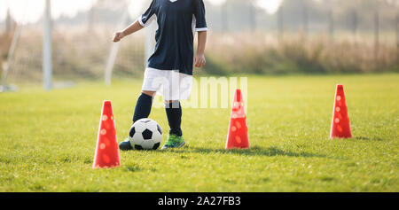 Fußball-Spieler Dribbling durch die Kegel in den Boden an einem sonnigen. Jungen Fußball (Fußball) Spieler dribbeln durch Kegel Stockfoto