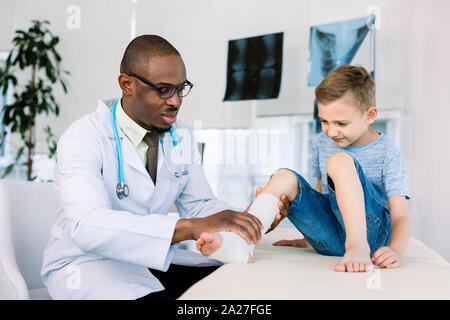 Kommt zum Arzt. Kleine Schule junge kommen zu afrikanischer Mann Arzt, nachdem er sein Bein gebrochen in der Straße. Bein im Verband Stockfoto