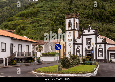 Platz geteilt durch Gras Insel mit einem Verkehrsschild, von Häusern umgeben. Typisch portugiesische weißen Kirche. Wald auf einem Hügel im Hintergrund. Faial d Stockfoto