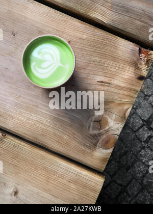 Matcha grüner Tee Latte in Einweg Karton takeaway Cup auf rustikalen Holztisch im Freien, text Raum Stockfoto