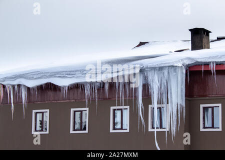 Große Eiszapfen hängen vom Dach des Gebäudes. Kaltes Wetter und starker Schneefall Stockfoto