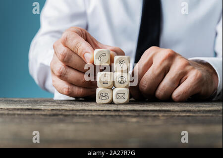 Geschäftsmann stapeln Holz- Würfel mit Kontakt und Informationen Symbole auf Sie auf rustikalen Holztisch. Stockfoto