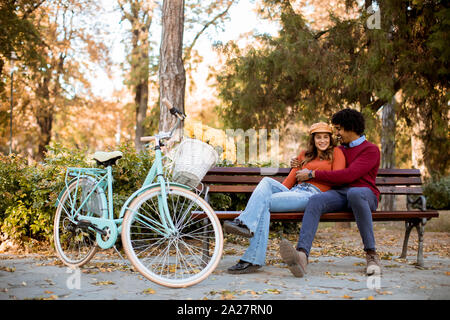 Multiratial junge Liebende Paar sitzt auf der Bank im Herbst City Park Stockfoto